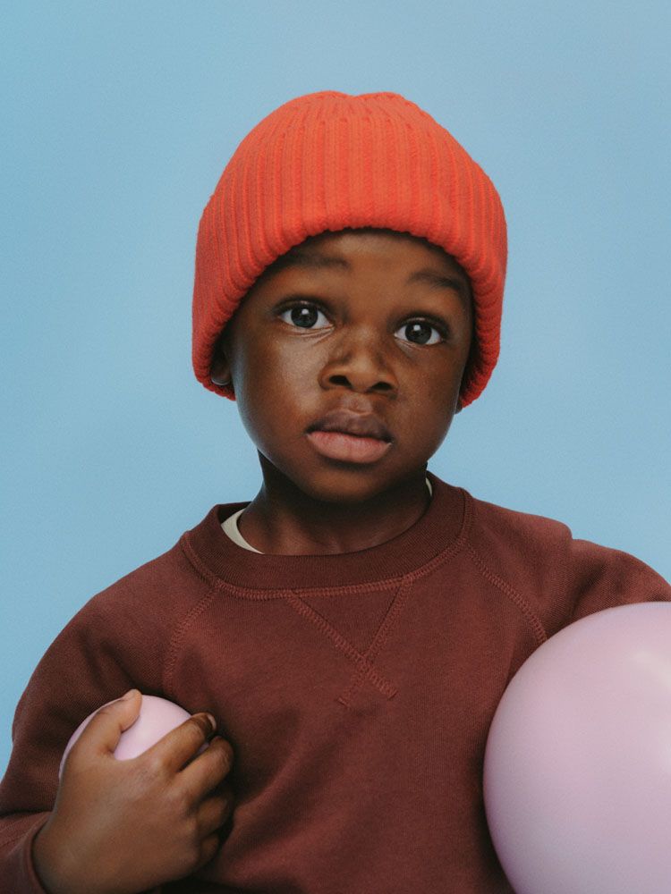 A boy in an orange beanie holding pink balloons