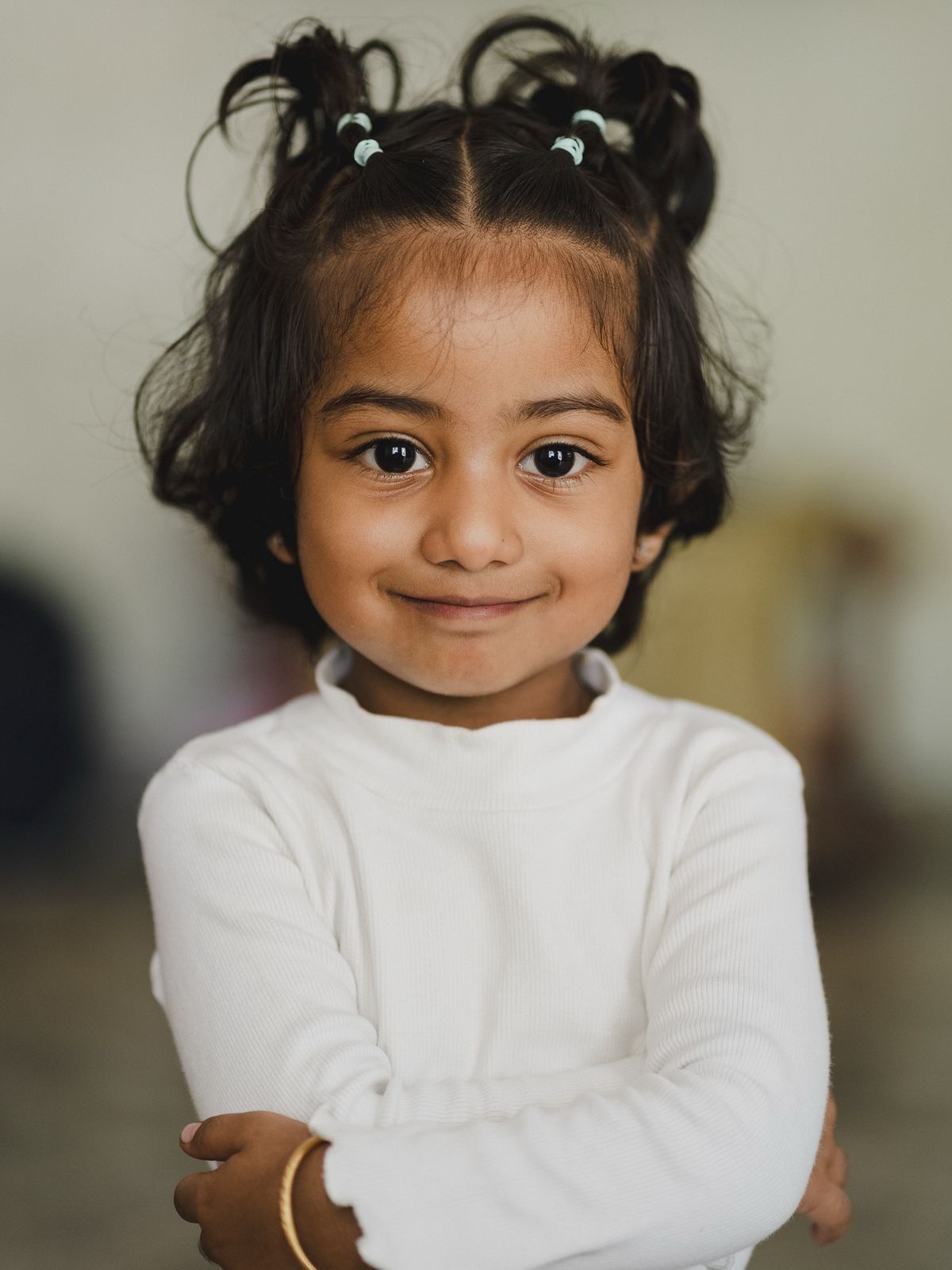 A smiling young girl with pigtails, arms folded