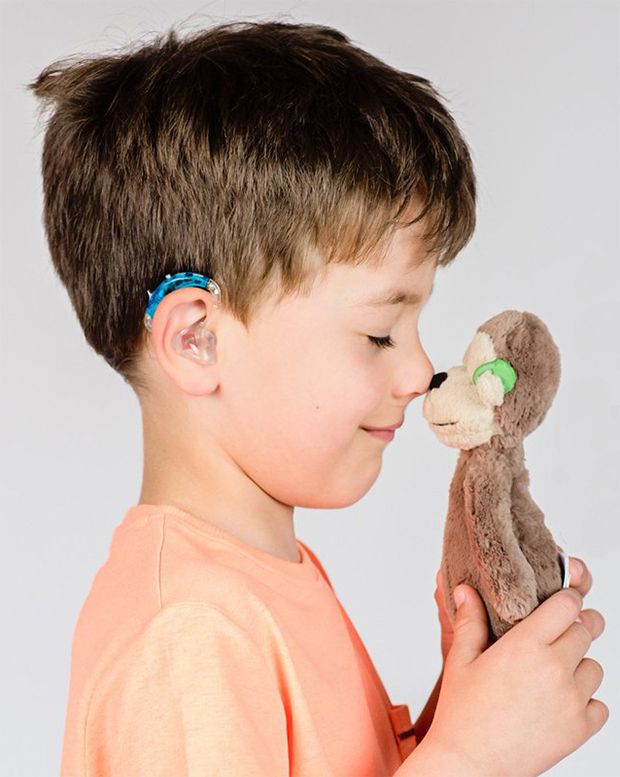 A boy with a hearing aid touching noses with his plush monkey