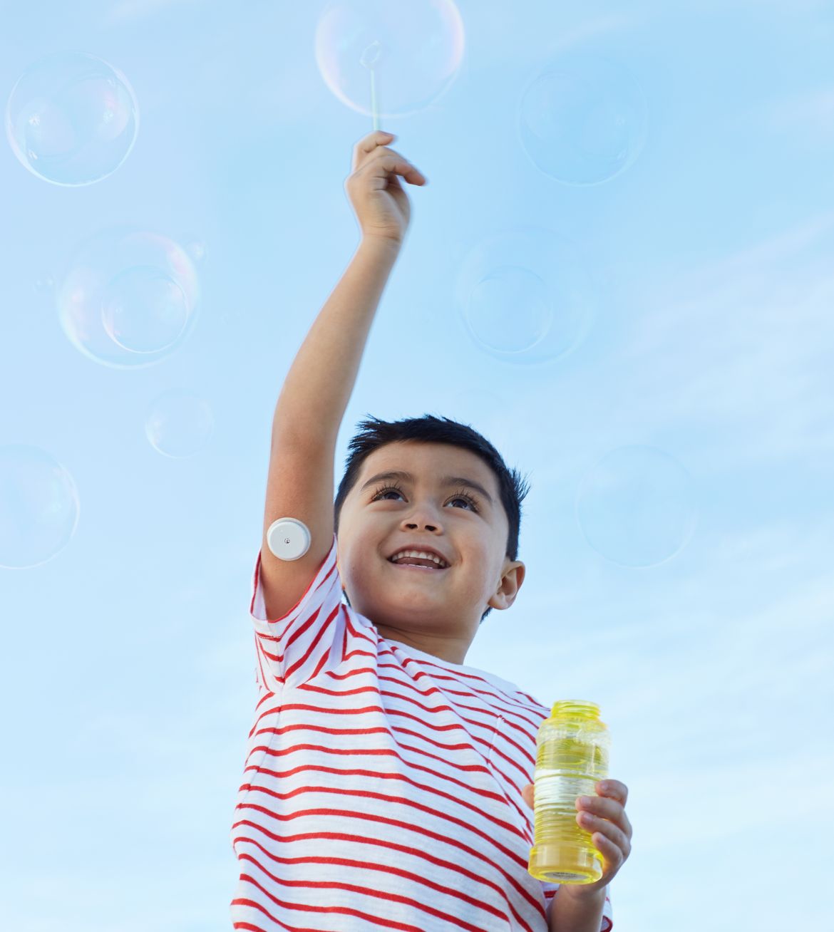 A smiling boy blowing bubbles against a bright sky