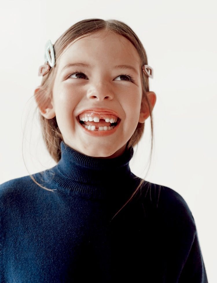 A laughing girl in a navy turtleneck with hair clips