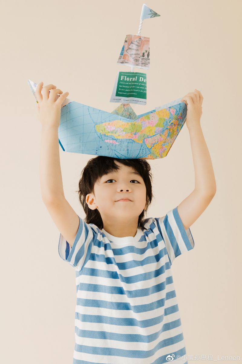 A boy balancing a paper boat made from a map on his head
